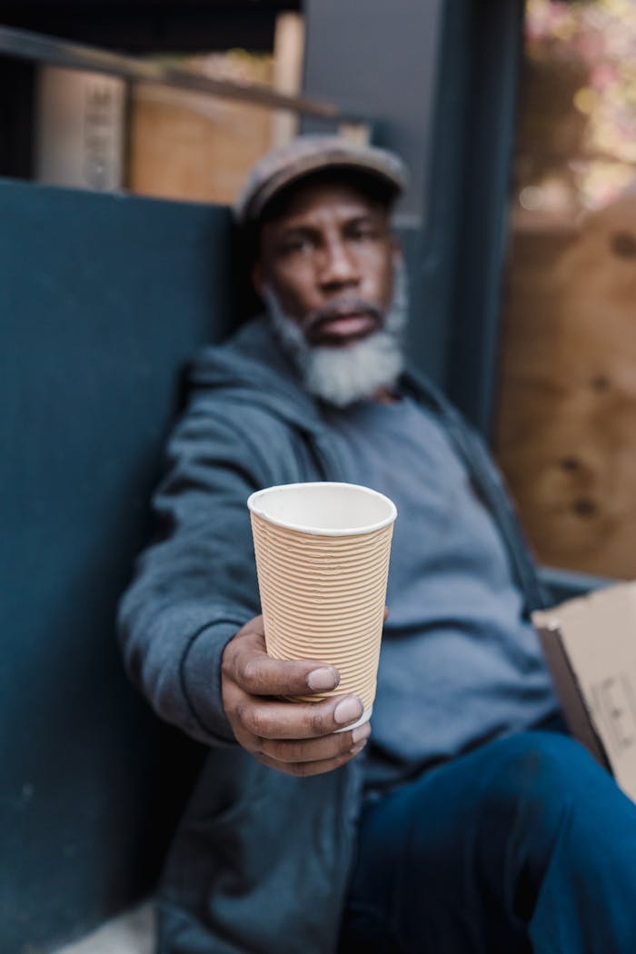 A man extends a cup for help, symbolizing hope and need on the streets.